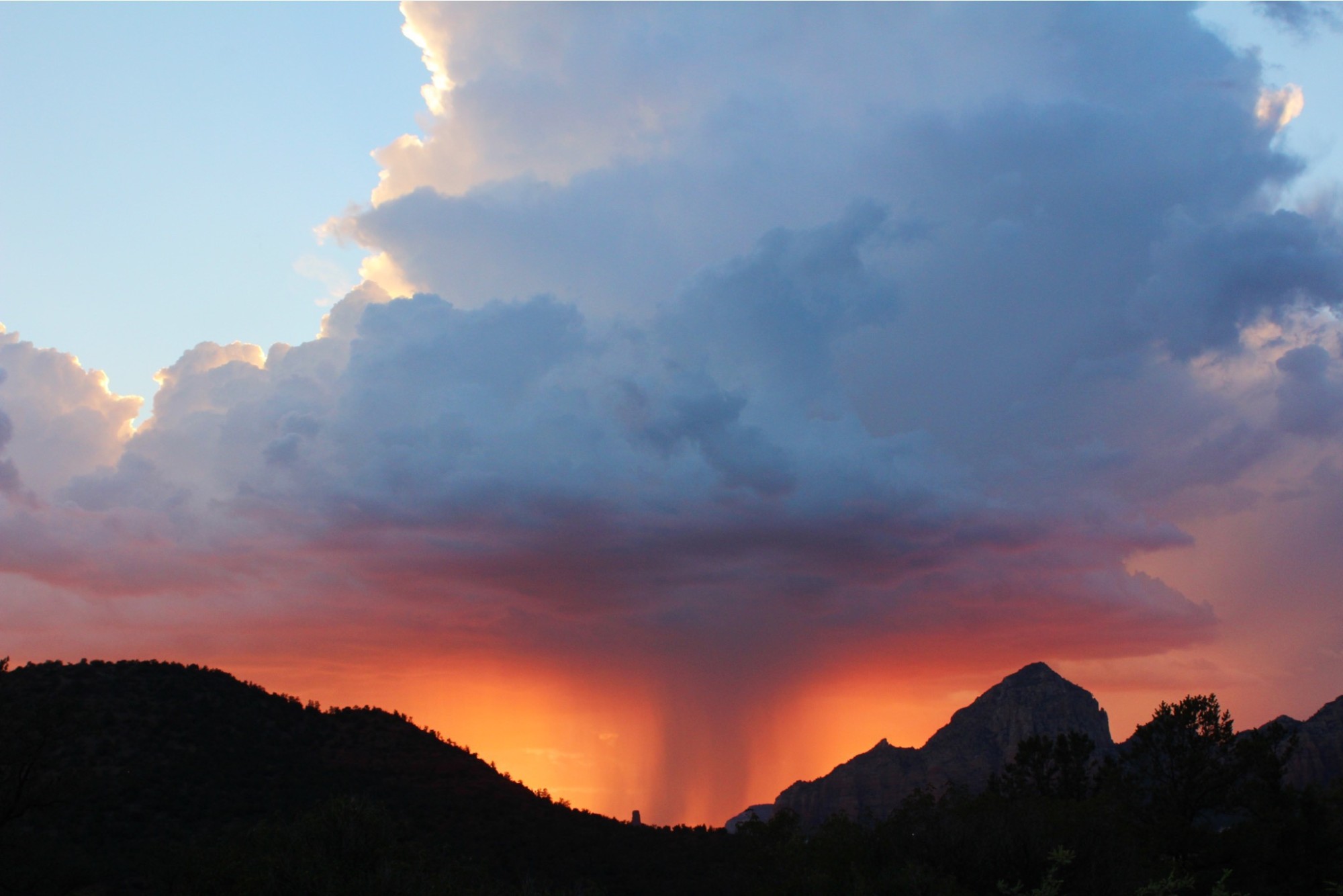 Storm clouds glowing orange over mountains at sunset