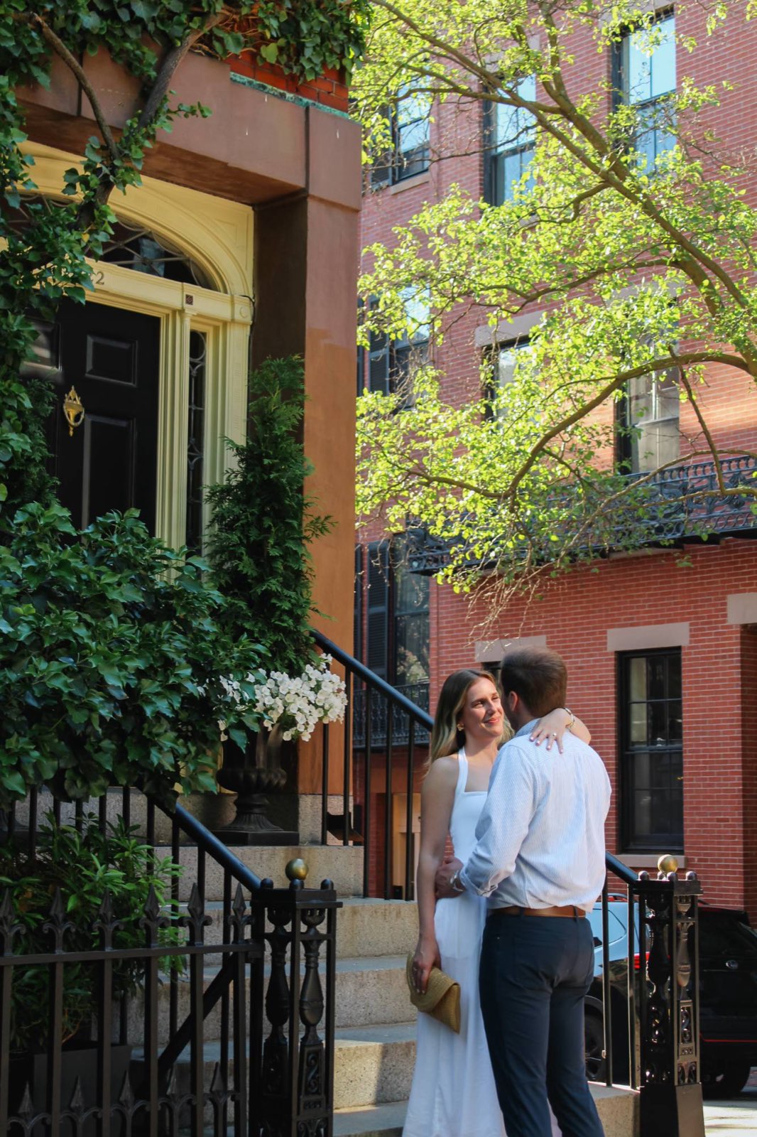 Couple embracing beside an ivy-covered stoop with white flowers and iron railings in Beacon Hill, Boston
