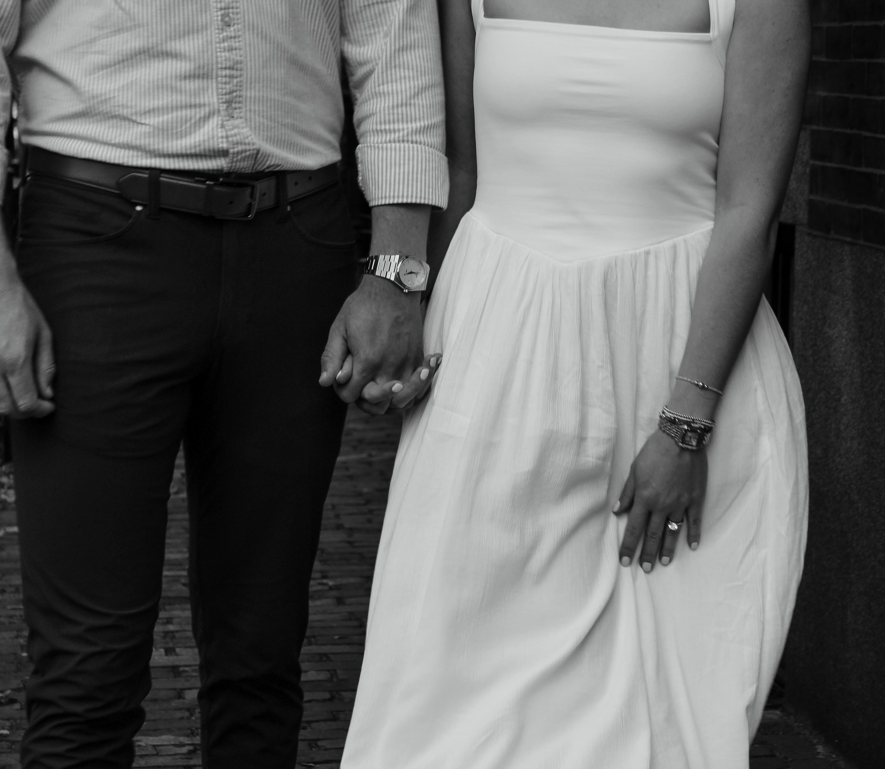 Black-and-white photo of a couple holding hands, her in a white sundress