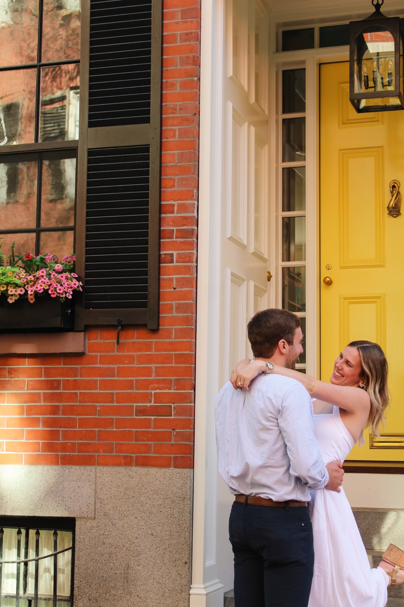 Engaged couple embracing in front of a yellow door in Beacon Hill, Boston