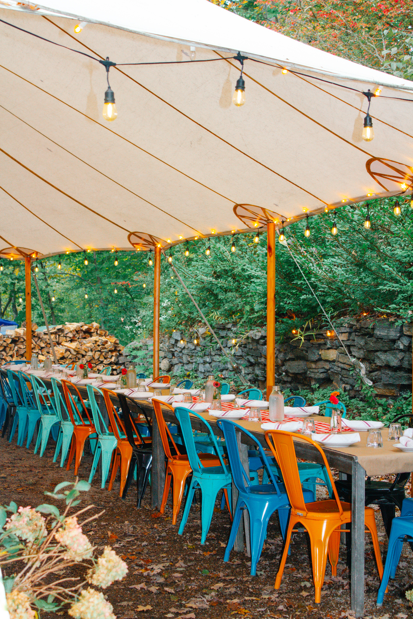 Long outdoor tables lined with colorful metal chairs under a string-lit tent at Otto Pizza in Chester, Connecticut
