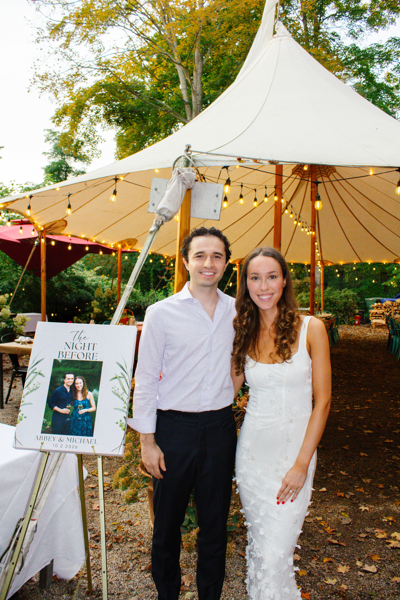 Couple standing beside a “The Night Before” welcome sign under the tent at Otto Pizza in Chester, Connecticut