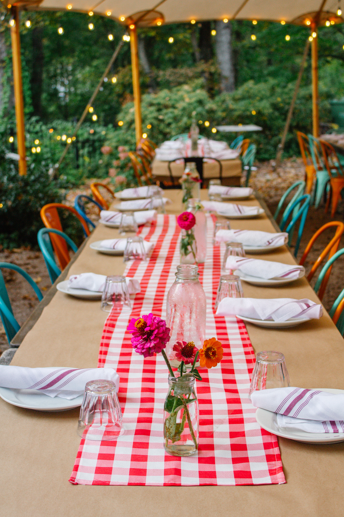 Red gingham table runner, zinnias in glass jars and place settings at a welcome dinner at Otto Pizza, Chester