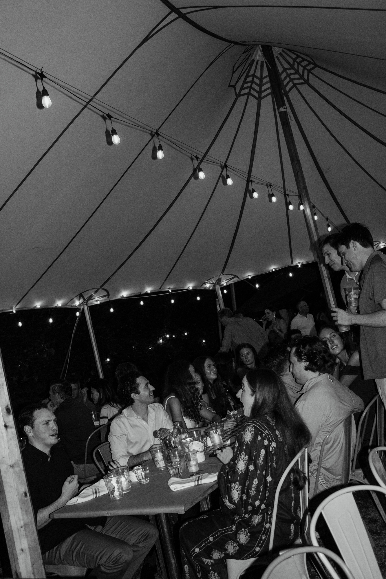 Black-and-white photo of guests gathered around candlelit tables under the tent at Otto Pizza in Chester, Connecticut
