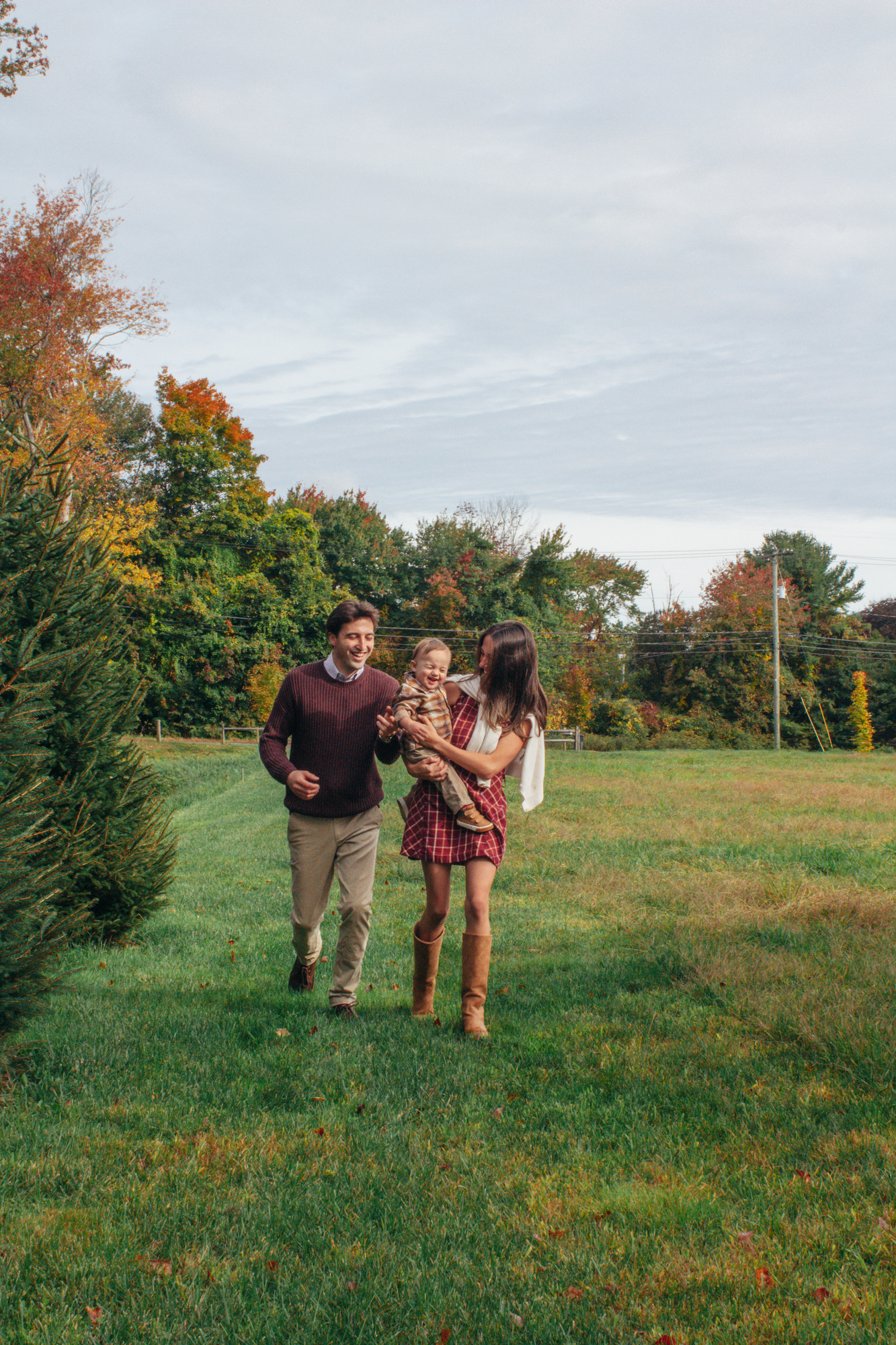 Family of three laughing as they walk across a green field with fall foliage at Silverman's Farm in Easton, Connecticut