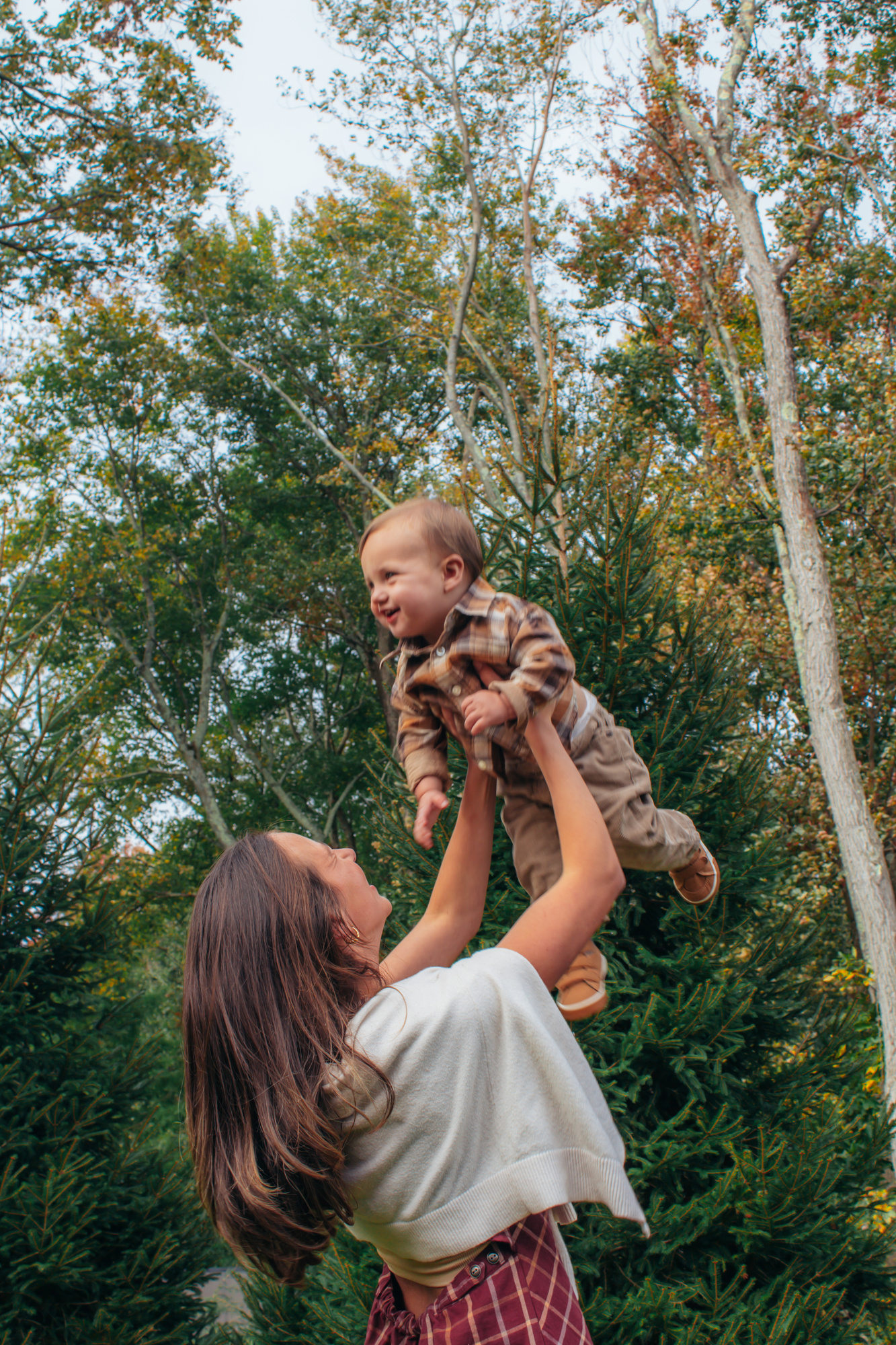 Mother lifting her laughing son high into the air beneath autumn trees at Silverman's Farm, Easton
