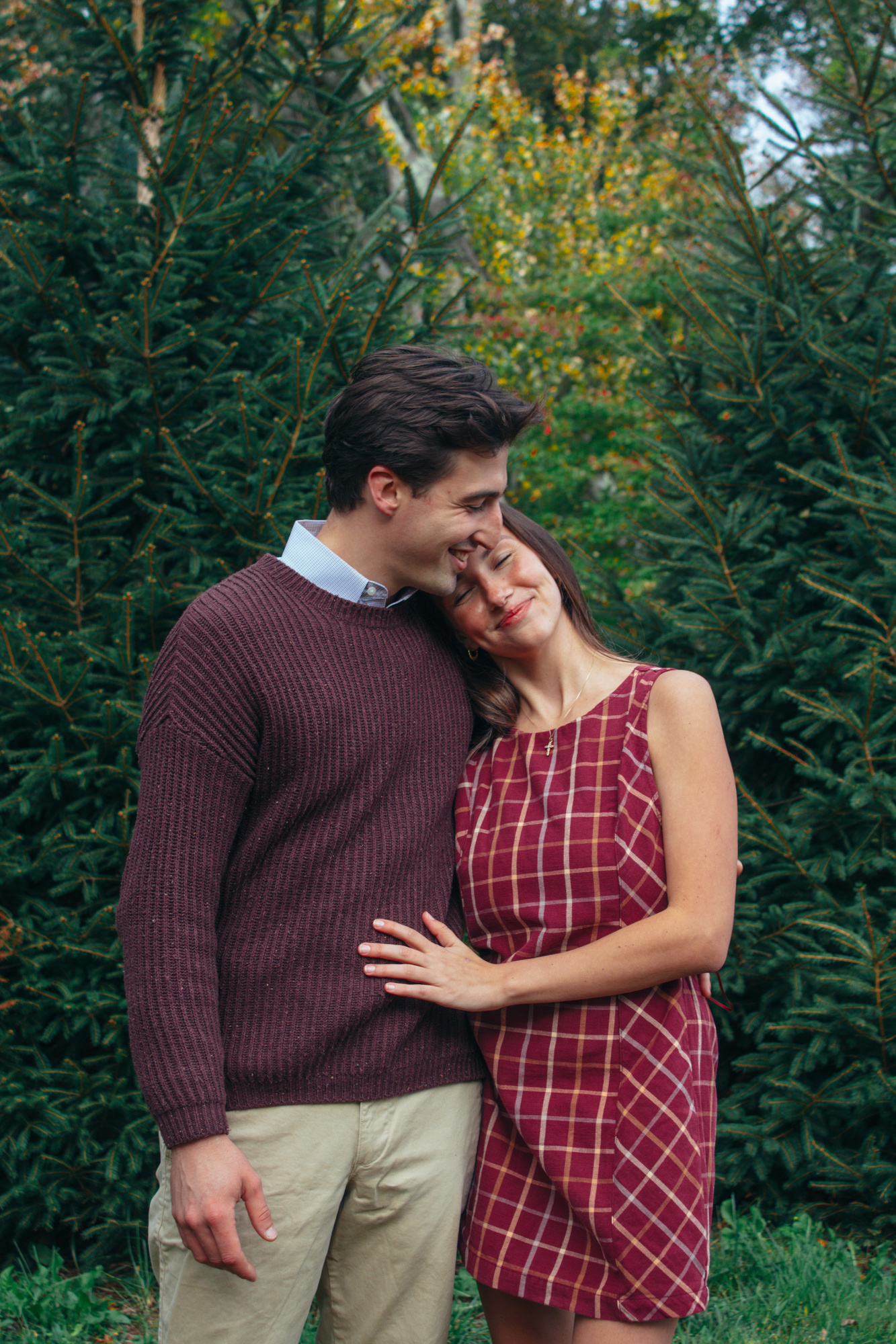 Couple embracing in front of evergreen trees during their family session at Silverman's Farm, Easton
